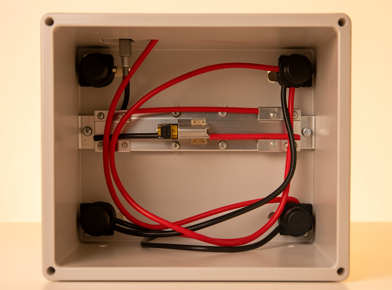 Tidy LiFePO4 battery enclosure interior with red and black DC cables routed through black cable glands, busbars and fuse visible