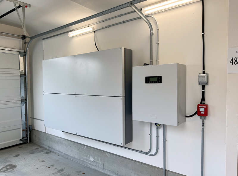 A 48 volt LiFePO4 home battery bank wall-mounted beside a hybrid inverter in a garage